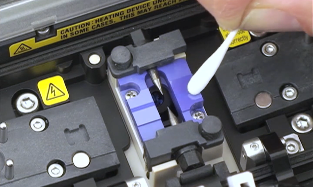 Technician performing fiber tool maintenance by cleaning splicer V-grooves